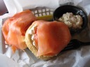 A bagel with cream cheese, lox, tomato, onion, and capers, alongside 
potato salad.
