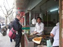 P buys fried dumplings from another shocked-looking Chinese man.  
A jian bing is in the foreground in the process of being made.
