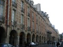 Surrounding each side of the square is the same set
of brick and stone buildings, continuing the symmetry of the square
itself.  

These were in the background of the previous picture.


They have dormer windows at the top and arcade at the bottom.
